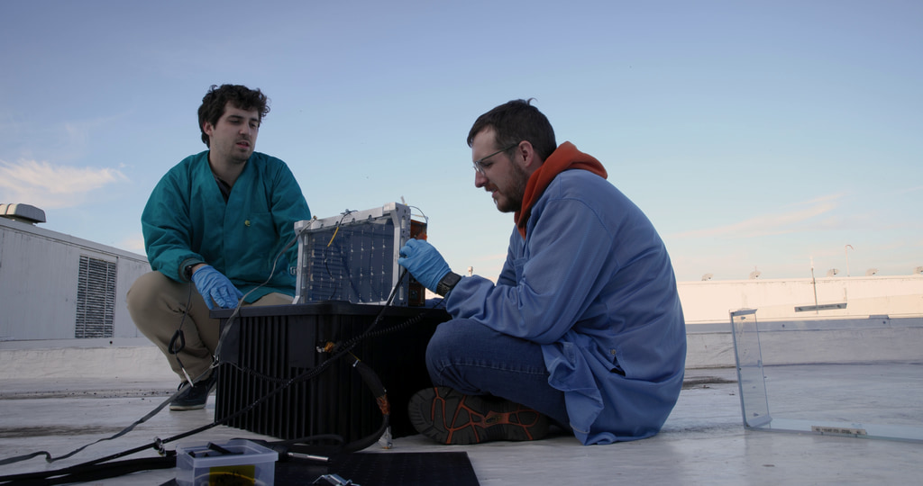 This video shows engineers conducting an open-sky test of the BurstCube satellite’s GPS at NASA’s Goddard Space Flight Center in Greenbelt, Maryland. The first shot shows Benjamin Nold (NASA) and Justin Clavette (SSAI) sitting around the spacecraft on a rooftop while Kate Gasaway (NASA) works in the background. The second shot shows Gasaway and Clavette looking at a laptop in the background, with BurstCube in the foreground. The third shot shows birds landing on an antenna on the rooftop. The fourth shot shows Clavette and Nold crouched next to the BurstCube satellite. The fifth shot shows Gasaway typing on the laptop. The sixth shot is a closer view of Gasaway and Clavette looking at the laptop. The eighth shot shows some of the electronics used to monitor the spacecraft. The ninth shot shows the data readout from the spacecraft on the laptop. The final shots show birds flying over the rooftop.
Credit: NASA/Sophia Roberts
