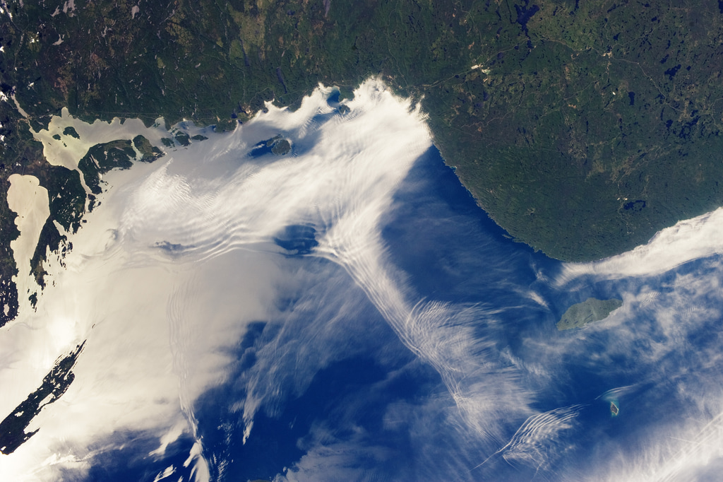 From the vantage point of the International Space Station, astronauts frequently observe atmospheric and surface phenomena in ways that are impossible to view from the ground. Two such phenomena—gravity waves and sunglint—are illustrated in this photograph of northeastern Lake Superior.Gravity waves are produced when moisture-laden air encounters imbalances in air density, such as might be expected when cool air flows over warmer air. This can cause the flowing air to oscillate up and down as it moves, causing clouds to condense as the air rises and cools and to evaporate away as the air sinks and warms. This produces parallel bands of clouds oriented perpendicular to the wind direction. The orientation of the cloud bands in this image, parallel to the coastlines, suggests that air flowing off of the land surfaces to the north is interacting with moist, stable air over the lake surface, creating gravity waves.Caption by William L. Stefanov, Jacobs/JETS and Michael H. Trenchard, Barrios/JETS, both at NASA-JSC. Image Credit: NASA/ISS