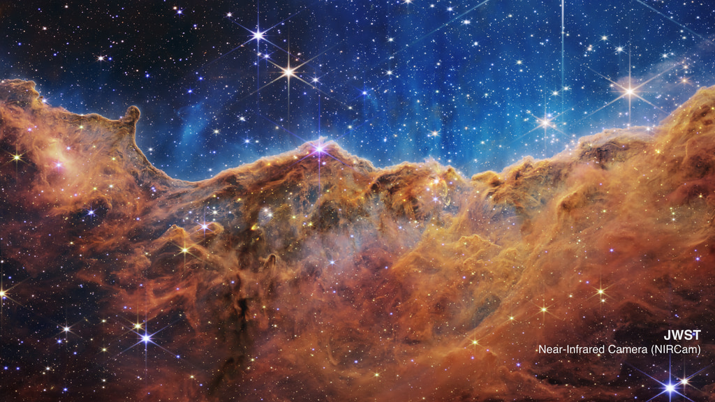 The seemingly three-dimensional “Cosmic Cliffs” showcases Webb’s capabilities to peer through obscuring dust and shed new light on how stars form. Webb reveals emerging stellar nurseries and individual stars that are completely hidden in visible-light pictures. This landscape of “mountains” and “valleys” is actually the edge of a nearby stellar nursery called NGC 3324 at the northwest corner of the Carina Nebula. So-called mountains — some towering about 7 light-years high — are speckled with glittering, young stars imaged in infrared light. A cavernous area has been carved from the nebula by the intense ultraviolet radiation and stellar winds from extremely massive, hot, young stars located above the area shown in this image. The blistering, ultraviolet radiation from these stars is sculpting the nebula’s wall by slowly eroding it away. Dramatic pillars rise above the glowing wall of gas, resisting this radiation. The “steam” that appears to rise from the celestial “mountains” is actually hot, ionized gas and hot dust streaming away from the nebula due to the relentless radiation. Objects in the earliest, rapid phases of star formation are difficult to capture, but Webb’s extreme sensitivity, spatial resolution and imaging capability can chronicle these elusive events.
